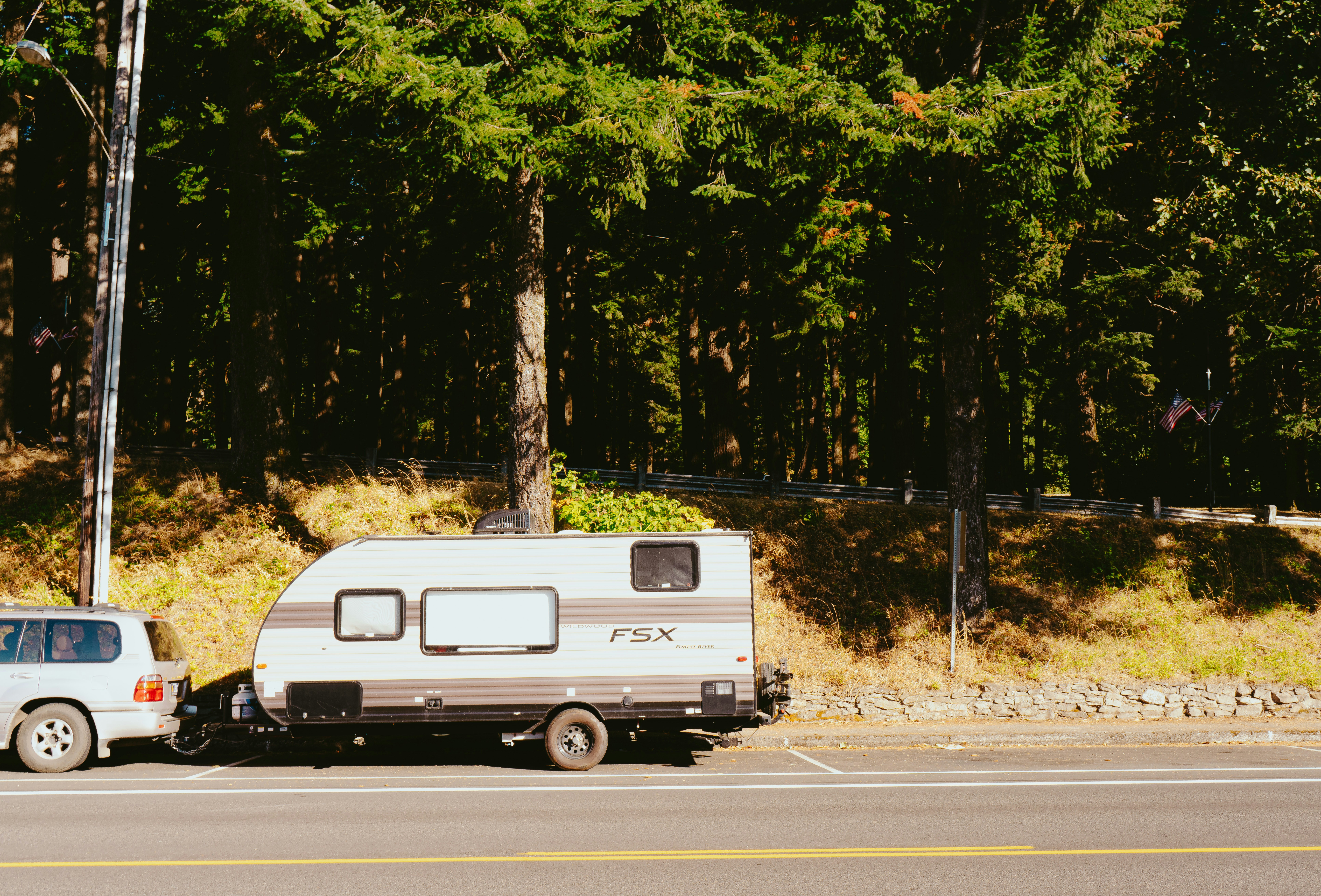 SUV towing a small FSX travel trailer along a sunny forest road.
